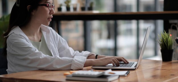Hermosa joven asiática sentada en una cafetería usando una computadora portátil feliz joven mujer de negocios sentada en una mesa en una cafetería con una computadora tab top