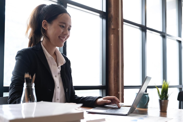 Hermosa joven asiática sentada en la cafetería usando una computadora portátil