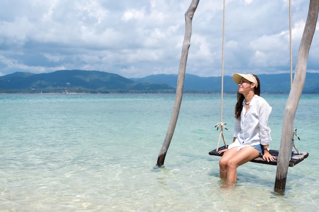 Una hermosa joven asiática sentada en un columpio en el mar con fondo de cielo azul