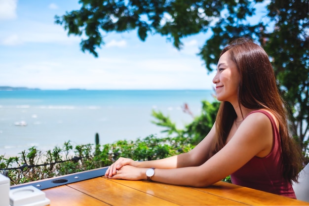 Una hermosa joven asiática sentada y mirando el mar y el cielo azul