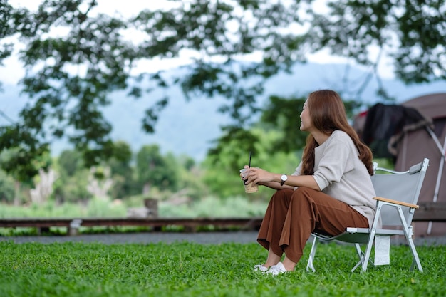 Una hermosa joven asiática sentada en una silla de camping con una carpa en el parque