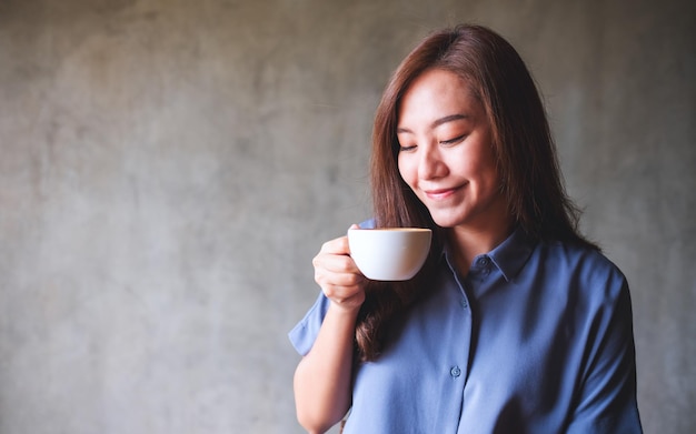 Una hermosa joven asiática sosteniendo y bebiendo café caliente en la cafetería