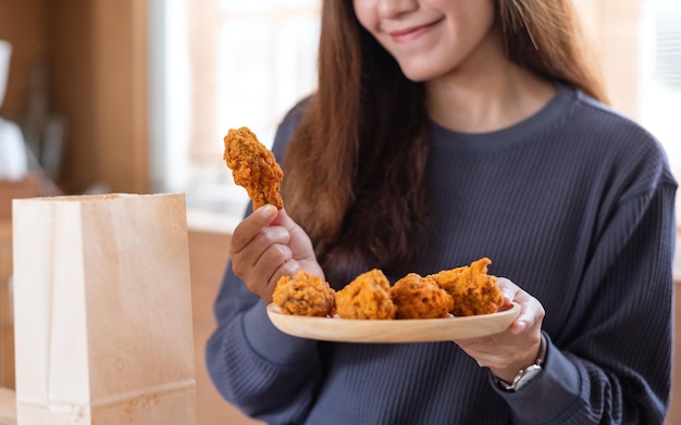 Una hermosa joven asiática sosteniendo un plato de pollo frito en la cocina de casa