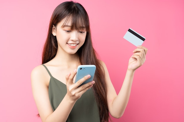 Hermosa joven asiática con teléfono en la pared rosa