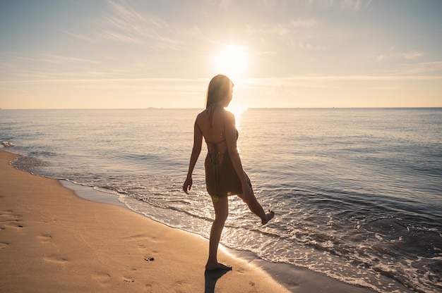 Hermosa joven asiática en traje de baño disfrutando y chapoteando en la playa en el mar tropical por la mañana