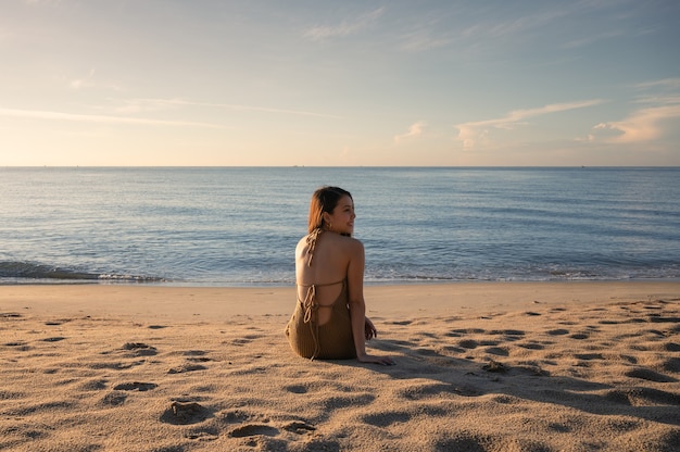 Hermosa joven asiática en traje de baño sentado y tomando el sol en la playa con sol por la mañana