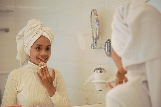 Hermosa joven asiática con túnica blanca maquillándose en el baño frente a un gran espejo