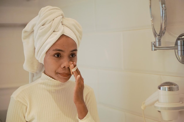 Hermosa joven asiática con túnica blanca maquillándose en el baño frente a un gran espejo