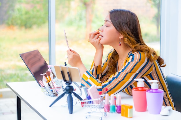 Hermosa joven asiática, vlogger, maquillándose y revisando productos de belleza en un video blog en casa