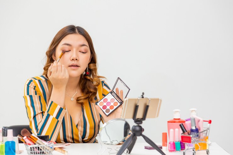 Foto hermosa joven asiática, vlogger, maquillarse y sombra de ojos mientras revisa productos de belleza en un blog de video en casa, espacio para espacio de copia