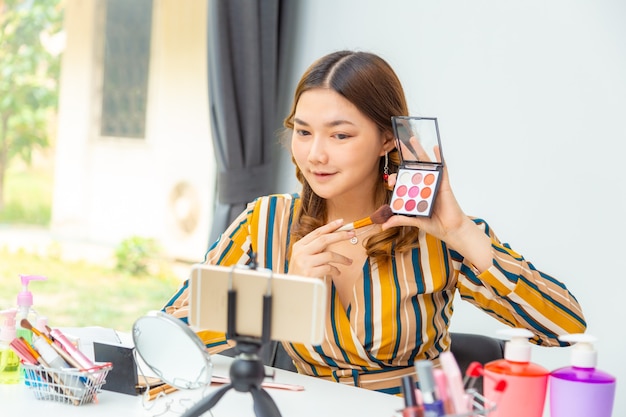 Hermosa joven asiática, vlogger, revisando productos de belleza en vivo en su video blog en casa