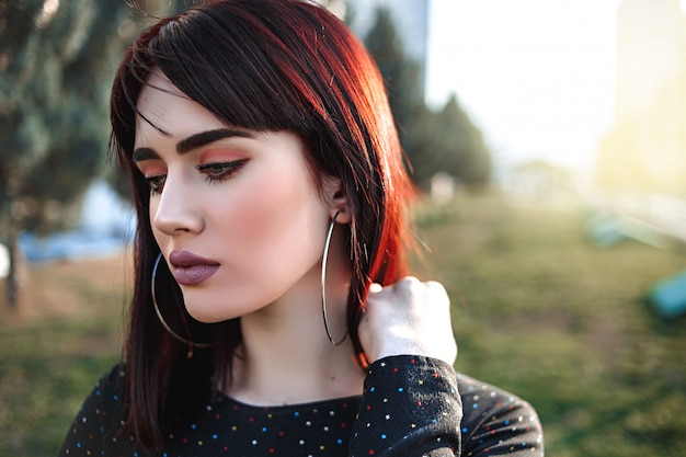 Hermosa joven con aspecto pesado y hosco en vestido negro fuera posando durante la puesta de sol