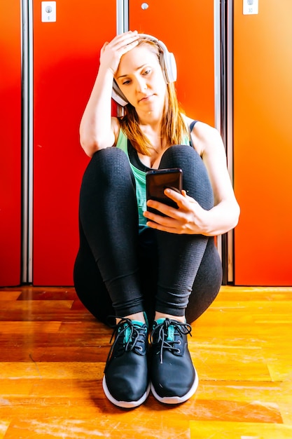 Hermosa joven atleta ajuste mujer mirando smartphone con auriculares de música en el vestuario del gimnasio