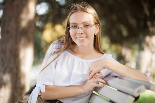 Foto hermosa joven atractiva con gafas sentado en el parque de otoño en el banco