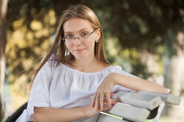 Foto hermosa joven atractiva con gafas sentado en el parque de otoño en el banco