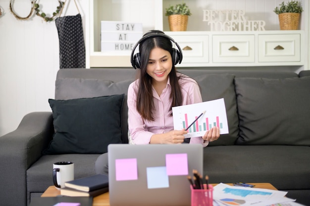 Una hermosa joven con auriculares está haciendo una videoconferencia a través de una computadora en casa durante la pandemia de coronavirus