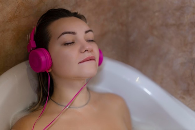 Hermosa joven con auriculares rosas relajándose en la bañera