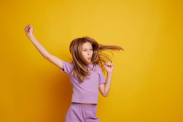 Una hermosa joven baila riéndose y divirtiéndose en un fondo amarillo limpio