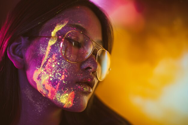 Hermosa joven bailando y haciendo fiesta con pintura fluorescente en su rostro. Retratos faciales de neón