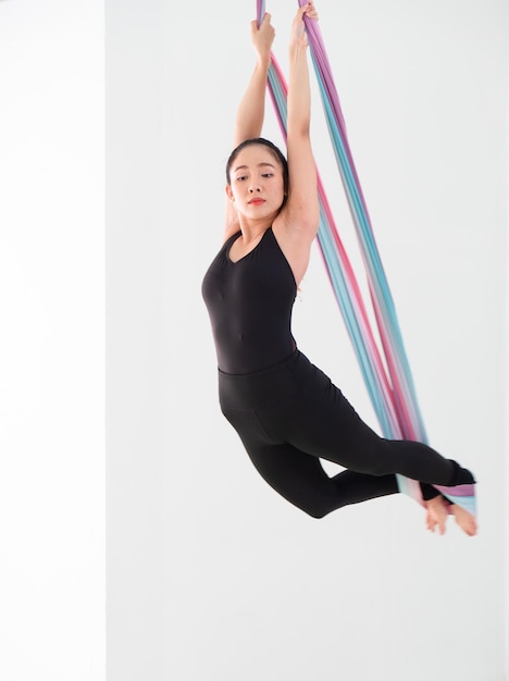 Hermosa joven bailarina asiática vestida de negro realizando danza aérea con telas multicolores en el estudioxA