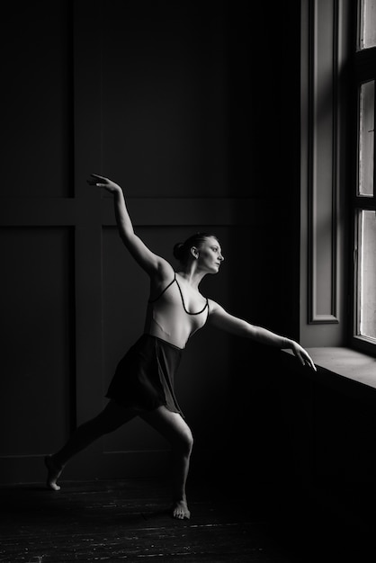 Hermosa joven bailarina de ballet clásico en pointe zapatos vistiendo un leotardo negro y falda en una pared de ladrillos