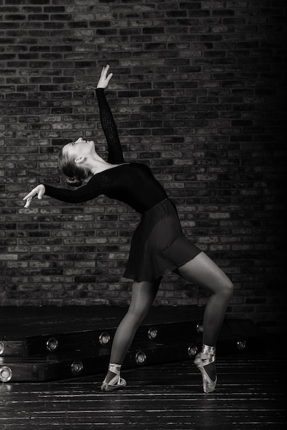 Hermosa joven bailarina de ballet clásico en zapatillas de punta con un leotardo negro y falda sobre un ladrillo