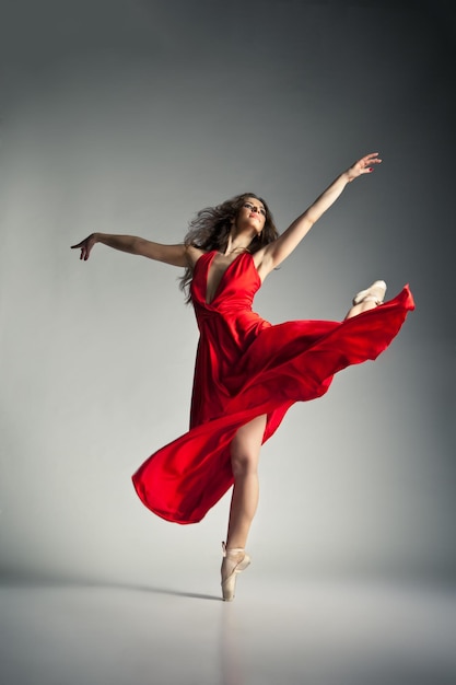 Hermosa joven bailarina de ballet con vestido rojo sobre fondo gris oscuro