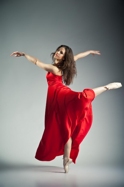 Foto hermosa joven bailarina de ballet con vestido rojo sobre fondo gris oscuro