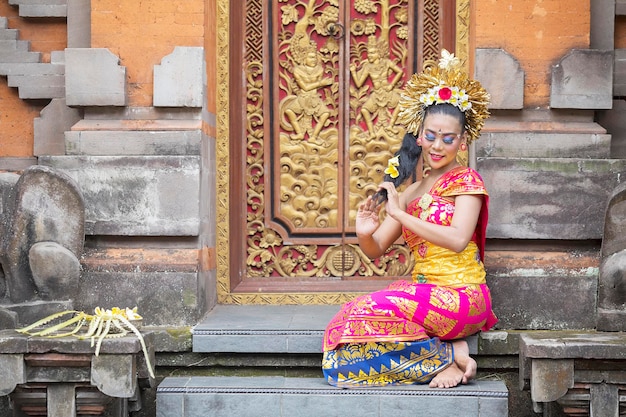 Hermosa joven balinesa sentada en la puerta de un templo con ropa tradicional