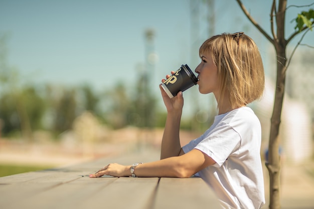 Una hermosa joven bebe café de un vaso de papel en el mostrador de un café al aire libre