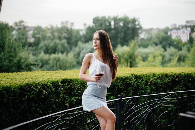 Hermosa joven bebe vino en la terraza de una hermosa casa. Fiesta.