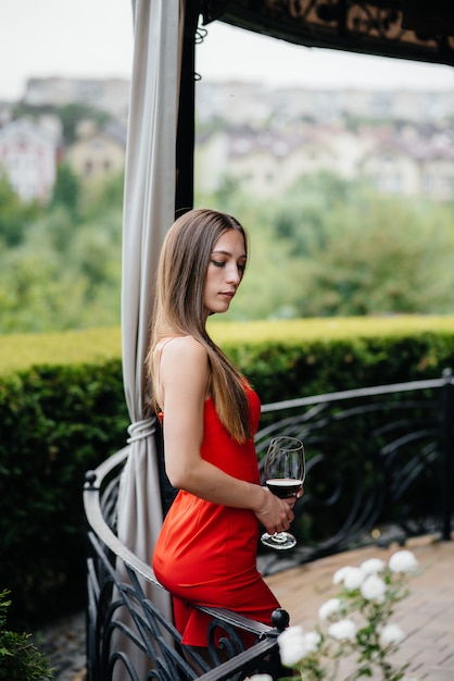 Hermosa joven bebe vino en la terraza de una hermosa casa. Fiesta.