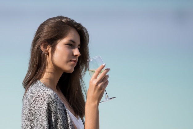 Hermosa joven bebe vino de un vaso.