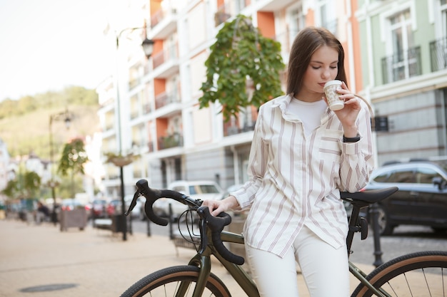 Hermosa joven bebiendo café, apoyado en su bicicleta, descansando después de montar