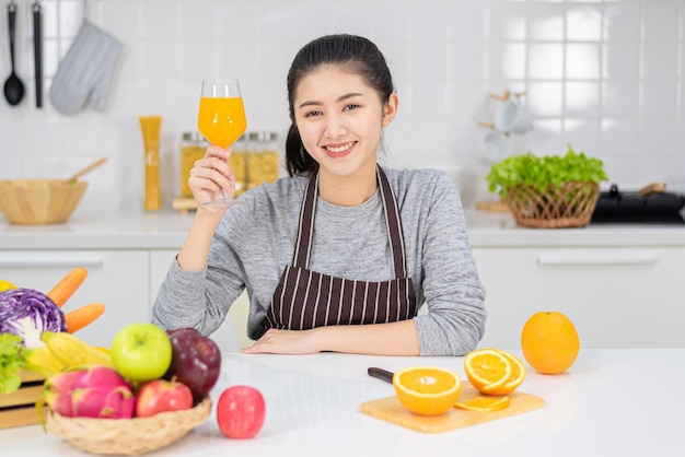 Hermosa joven bebiendo jugo de naranja fresco en la cocina. Dieta saludable