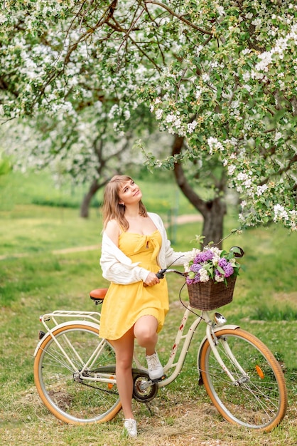 Foto una hermosa joven con una bicicleta retro camina en un jardín en flor en primavera disfruta del aroma de los manzanos en flor.