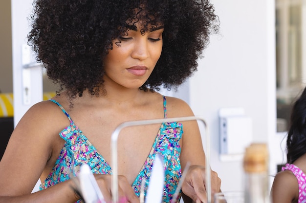 Hermosa joven birracial con cabello afro y vestido azul almorzando mientras está sentada en casa