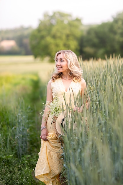 Hermosa joven con bolso trenzado, sombrero de paja y color de ramo en el campo