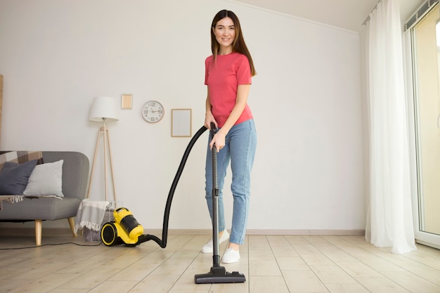 Hermosa joven de buen humor hace limpieza de la casa con una aspiradora