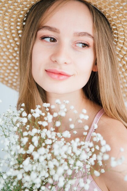 Hermosa joven con cabello largo y sombrero posando con un ramo de flores blancas. Viraje.