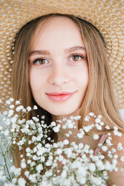 Hermosa joven con cabello largo y sombrero posando con un ramo de flores blancas. Viraje.