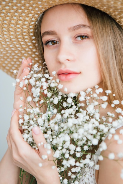 Hermosa joven con cabello largo y sombrero posando con un ramo de flores blancas. Viraje.