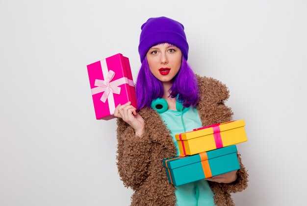 Hermosa joven con cabello morado en chaqueta con cajas de regalo navideñas.