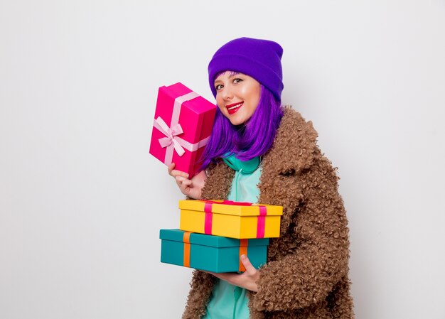 Hermosa joven con cabello morado en chaqueta con cajas de regalo navideñas.