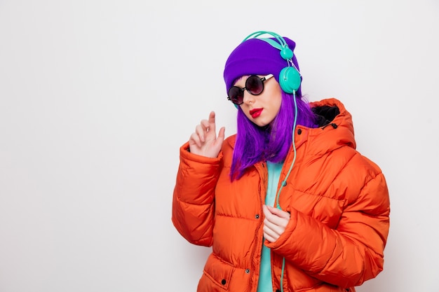 Hermosa joven con cabello morado y chaqueta naranja escuchar música en auriculares.