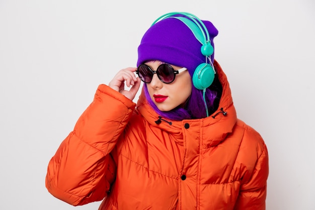 Hermosa joven con cabello morado y chaqueta naranja escuchar música en auriculares.