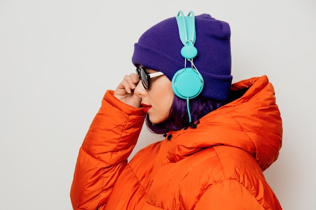 Hermosa joven con cabello morado y chaqueta naranja escuchar música en auriculares.