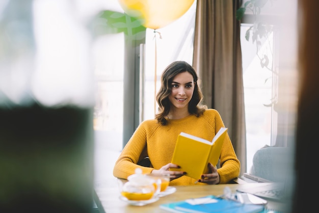 Hermosa joven de cabello oscuro con suéter amarillo cálido con libro en las manos