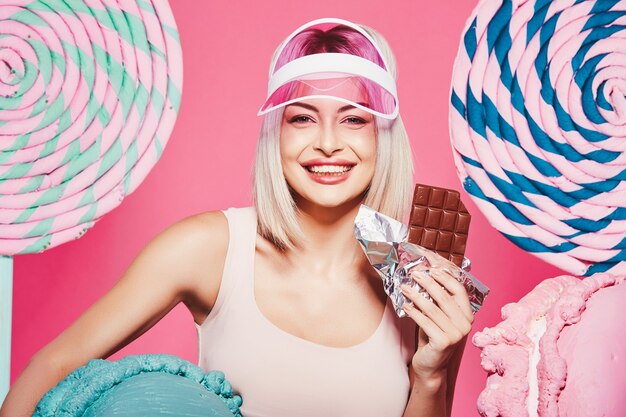 Hermosa joven con cabello rubio vistiendo top y falda de pie con enormes paletas dulces en rosa