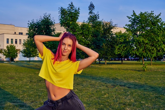 Hermosa joven con cabello teñido de rosa, top corto amarillo en el parque de la ciudad